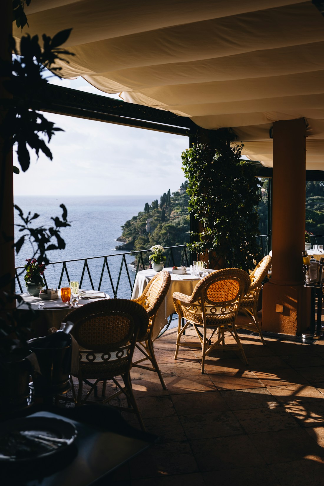 Sunlit restaurant terrace with woven chairs and linen-covered tables overlooking the sea in Portofino